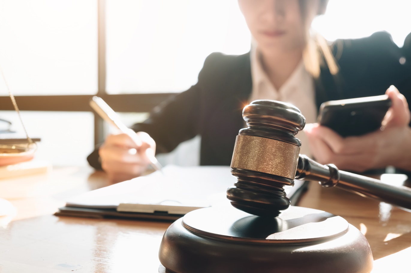 Business woman and lawyers discussing contract papers with brass scale on wooden desk in office and holding smartphone. Law, legal services, advice, Justice and real estate concept.